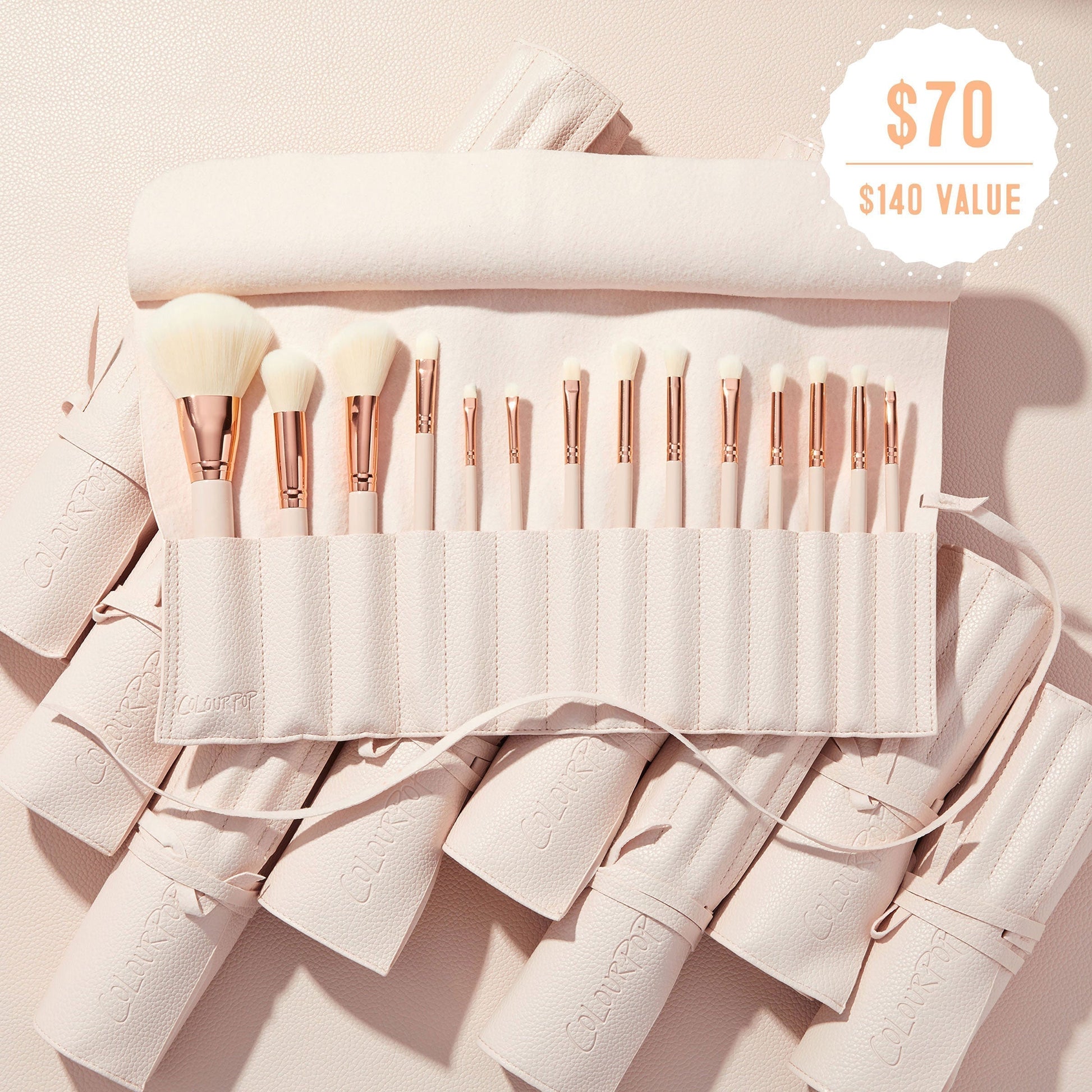 Sweet Fantasy ColourPop Shadow Palette & Brush Set brush roll opens to reveal soft white-bristle face and eye brushes with rose-gold ferrules, arranged in a blush-pink travel case on a textured nude surface, with a $70 ($140 value) badge.