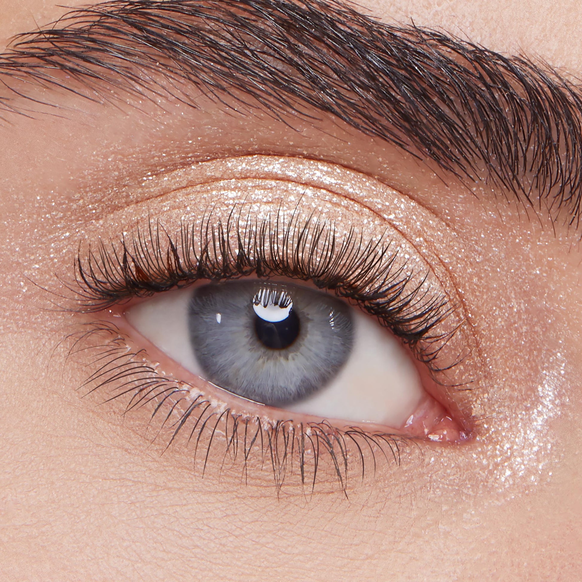 Ladybird Super Shock Shadow by ColourPop shimmering on eyelid - sparkly champagne-beige glitter eyeshadow swept across lid and inner corner for a metallic glow - shown in a close-up eye with long lashes and a defined brow.