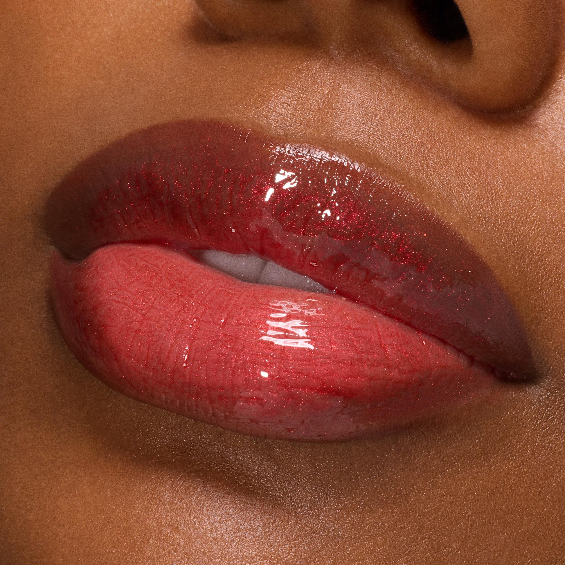 Glossy lips wearing Pack Member Lip Set, a sheer cherry-red tint with fine red shimmer and mirror shine on medium‑deep skin; close-up swatch highlights smooth, plump finish and sparkle for product detail; ColourPop Lip Set.